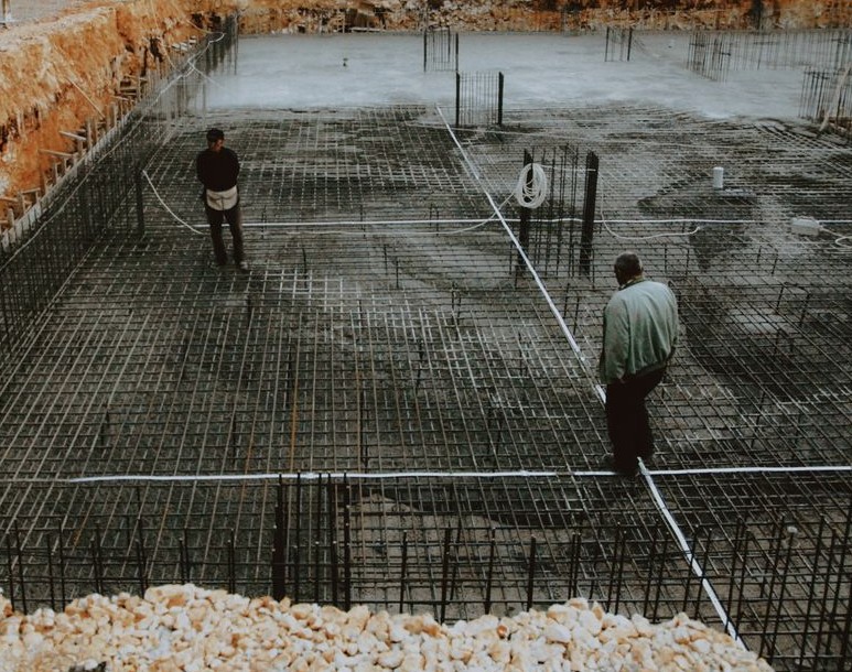 Concrete Slab and Foundation Installation, two workers inspecting a rebar grid foundation at a construction site