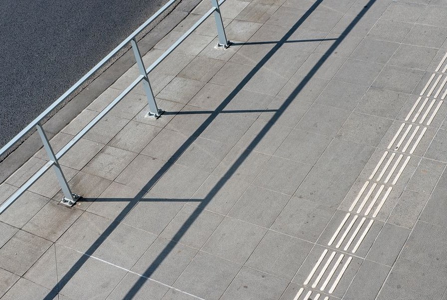 Aerial view of an urban sidewalk with metal railings casting long shadows